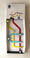 Full view of the multi hook hanger inside its box showing the colorful subway line design with attached hooks.