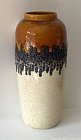 Full front view of the vase showing the three-tone glaze pattern: brown upper section, black textured lava band in the middle, and speckled off-white lower section.