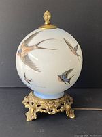 Front view of glass globe lamp showing hand painted swallows and brass base.