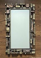 Full view of the Syroco mirror showing rectangular reflective glass surrounded by textured brutalist geometric frame in bronze and gold tones.