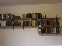 Wide shot of multiple wooden shelves mounted on the wall holding many vintage books, mostly hardcover, in varying sizes and colors.