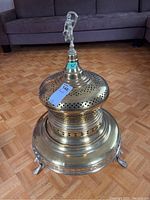 Full view of the tall brass brazier heater showing the rounded vented body and four ornate legs, with the decorative top and patina on the brass and copper surfaces