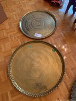 Both brass trays placed on parquet floor showing size difference and decorative pattern detail