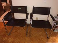 Pair of metal framed leather chairs side by side on parquet floor near boxes and wall outlet.