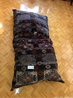 Two oversized square cushions stacked, showing geometric and floral patchwork pattern in earth tones.