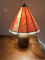 Full view of table lamp illuminated, showing orange stained glass shade and ceramic base