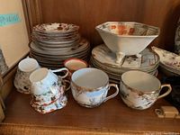 Shelved oriental ware tea set including teacups, saucers, plates, and bowls with floral and bird patterns.