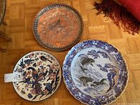 Overview of all three platters: two ceramic platters with Asian-themed fish and bird designs and one engraved copper platter with dragon motif.