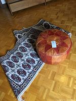 Round leather pouf sitting on two small woven carpets on wood floor