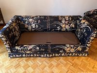 Front view of sofa with floral fabric upholstery and seat cushions removed revealing brown base area for pull-out bed.