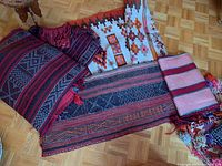 Cluster of folded and overlapping rugs showing various geometric patterns and colors including red, black, white, and orange
