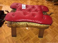 Red tufted saddle-shaped cushion on top of the foot stool, showing some wear on material
