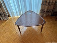 Full view of triangular teak table on parquet floor