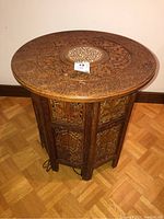 Full view of the carved sandalwood round table showing floral designs and folding base.