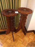 Pair of Indian sandalwood folding tables standing upright showing carved legs and round tops.