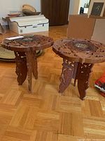 Two round Indian sandalwood folding tables with carved bases and detailed tops.