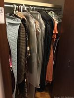 Closet view showing several hanging vintage women's clothing items including coats, dresses, and suits in various fabrics and patterns.