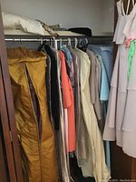 Photo of vintage women's clothing hanging in closet rack showing variety of dresses, suits, and evening wear mostly in neutral, pastel, gold and coral shades.