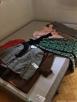 Multiple vintage jackets and pants spread on a mattress, showing various patterns including plaid and checkered