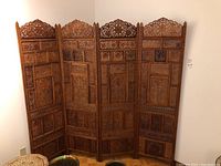 Full view of four-panel folding wooden screen standing against white wall, showing overall size and panel arrangement