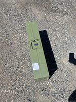 Photo of the folded green table placed vertically on gravel ground, showing the full compact rectangular form.