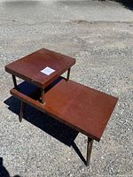 Full side view of the wooden two-tiered side table with brass supports on an outdoor gravel background.