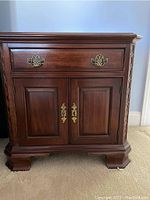 Front view of one Pennsylvania House dark wood night stand showing one drawer with brass handles and double-door cabinet below with brass keyhole escutcheons.