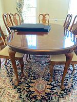 Photo of 8 wooden dining chairs around a matching table on patterned carpet, showing the style, wood finish and seat color.