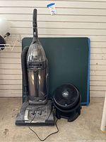 Photo showing Hoover WindTunnel upright vacuum, Vornado desk fan in front, and green card table in background.