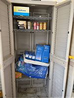 View of entire storage cabinet showing cans of soda, bottled water, and boxes of lightbulbs on shelves.
