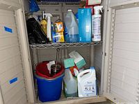 Shelf containing multiple household supplies including buckets, cleaning liquids, paper towels, and trash bags.