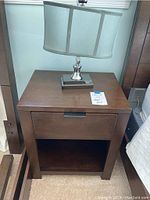 Front view of dark brown wooden night table with drawer and bedside lamp on top