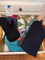 Top view of an open drawer containing various oven mitts, kitchen towels, and a digital grill timer.