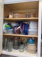 Lower shelves showing assorted plastic containers with colored lids (red, blue, purple, green) and stacks of plastic storage containers with lids. Includes various clear glass cups and bowls.