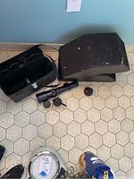 Two Klipsch stereo speakers and three Spiratone camera lenses, including telephoto, standard, and fisheye, with a black carrying case. Items arranged on the floor near scale and shoes.