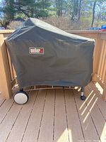 Grill covered with black vinyl cover featuring Weber logo on wooden deck