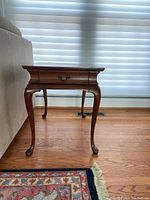 Side view of wood end table with curved legs and drawer.