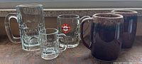 Photo showing all five mugs: 3 A&W glass mugs and 2 brown ceramic Hall mugs
