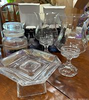 Photo showing clear glass color-changing hurricane candle holders and a geometric glass pedestal dish on a wooden table
