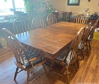 View of entire rectangular wooden dining table with leaf, surrounded by eight matching wooden dining chairs with spindle backs and cushions on some seats.