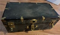 Closed view of black trunk shining with brass fittings on corners and lock area