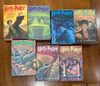 Front covers of all seven hardcover Harry Potter books displayed flat on a wooden surface illustrating the colorful original dust jackets with distinctive illustrations for each title.