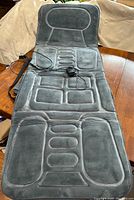 Full view of gray heated massage pad laid out flat with wired remote control and adapter