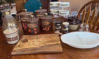 Overview of all items on a wooden table showing Pyrex canisters, ceramic canisters, carafe, cutting board and other small kitchenware.