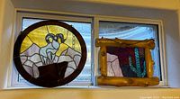 Two stained glass pieces: a round panel with big horn sheep on a mountain background and a rectangular cactus design in a wooden frame