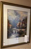 Full view of framed print depicting a mountain chapel scene, showing the ornate gold frame and matting.