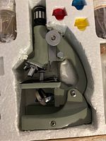 Front view of green metal body microscope with focusing knobs and multiple lenses in original foam case.