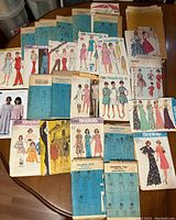 Overhead photo showing a spread of over 20 vintage and retro sewing pattern envelopes from brands like Simplicity, featuring various women's fashions from mid-20th century including casual and formal wear.