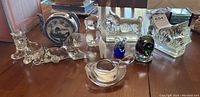 Image showing vintage clear glass Scotty dog bookends, blue and white ceramic teapot with scenic design, clear glass animal figurines, and colorful glass paperweights on wooden table.