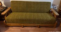 Front view of green upholstered wooden framed couch with wagon wheel design on sides